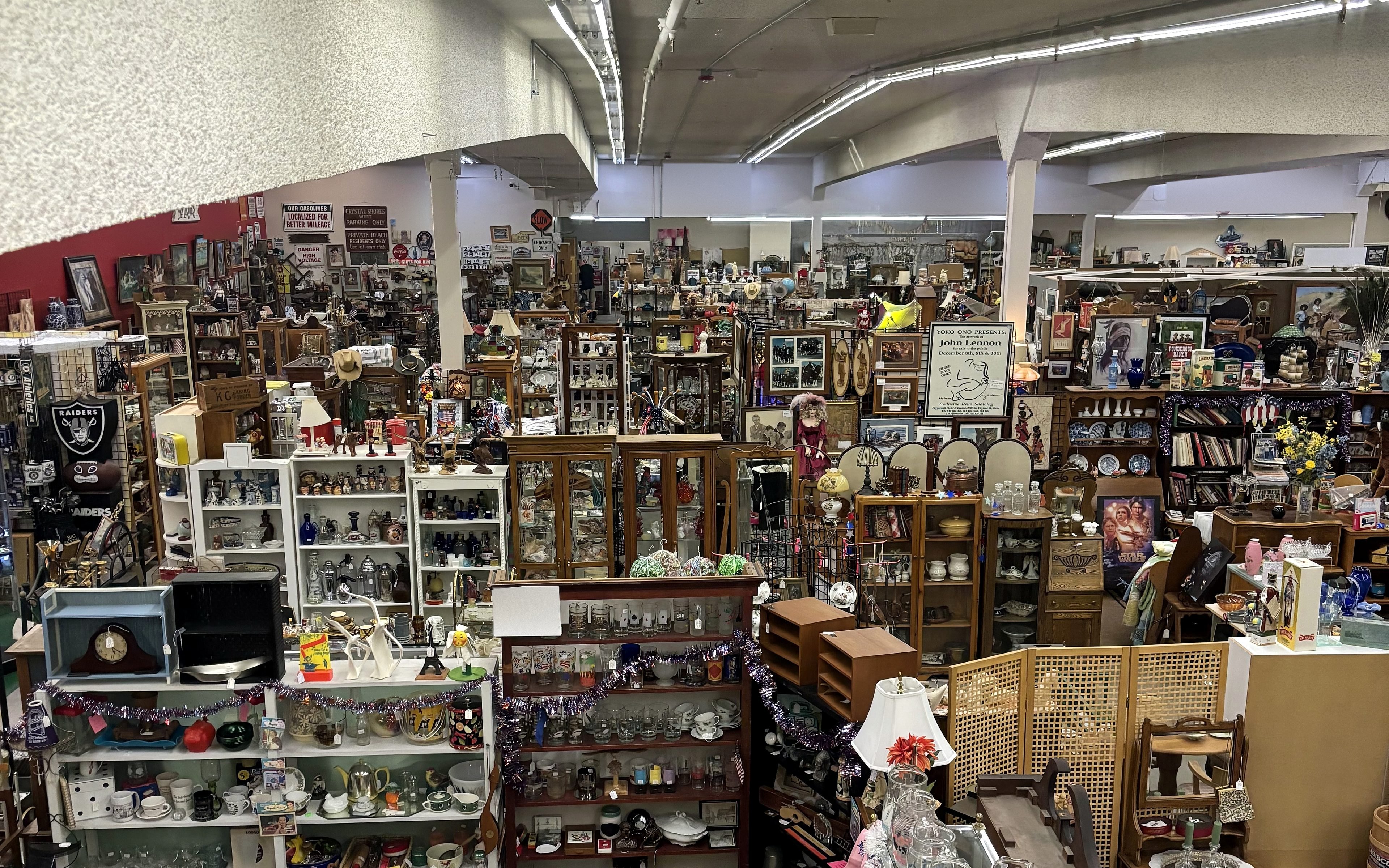 Inside Carson Antiques & Collectibles Mall — a long aisle of vendor booths stacked with glassware, ceramics, hutches and framed prints under the shop's high ceiling