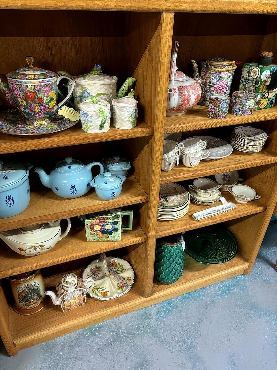 Teapots, a blue tea set, cups and saucers and floral china on oak shelves